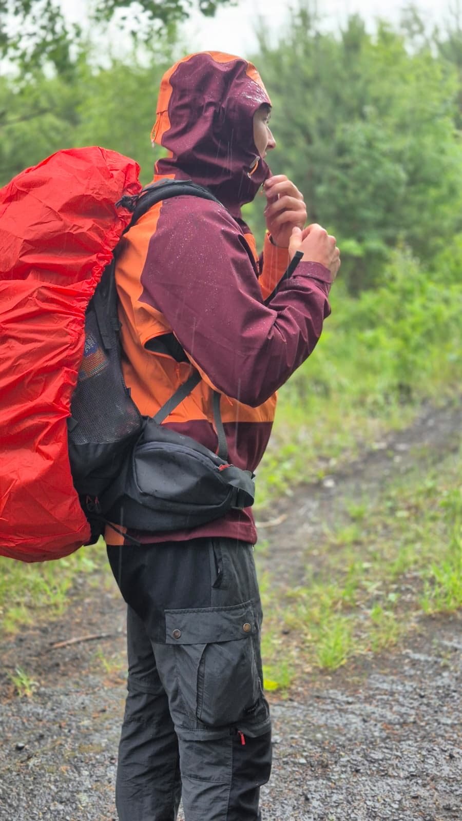 Product tester with the hood of the Ternua Klimmer Jacket closed, in the rain on a forest path