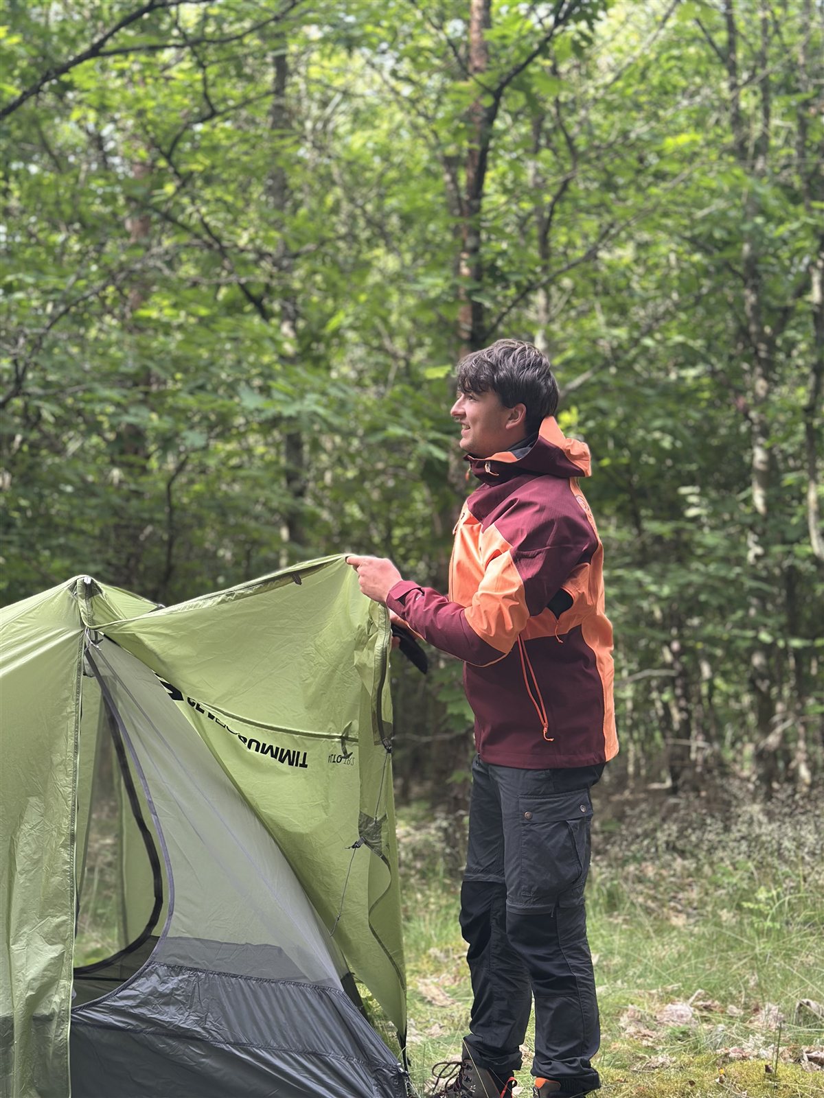 Product tester wearing the Ternua Klimmer Jacket while pitching a tent in the woods
